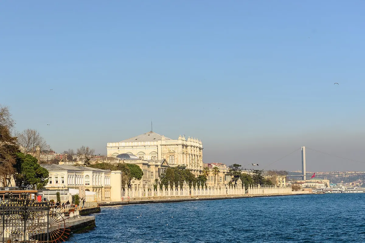 ボスポラス海峡沿いに長く続くDolmabahçe宮殿のクリーム色の水辺。手前にはモスク、遠景には橋が見えます。