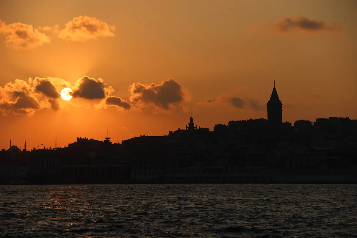 オレンジ色の夕焼け空を背景に、水面越しに浮かぶGalata Towerと旧市街のシルエット。