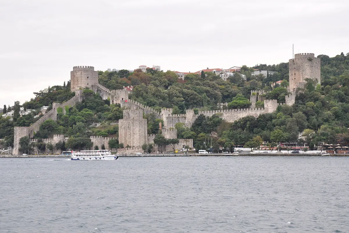 ボスポラス海峡を見下ろす木々の丘を登るRumeli Fortress。石の塔と長い狭間付きの城壁が連なります。
